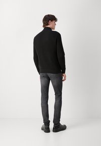 Maglione a costine nero con colletto alto, abbinato a jeans grigi scuri slim-fit e scarpe nere. Design semplice e strutturato.