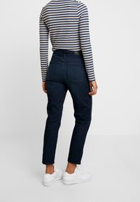 Mörka denimjeans med hög midja, avsmalnande ben och två bakfickor, i kombination med en randig långärmad topp och vita sneakers.