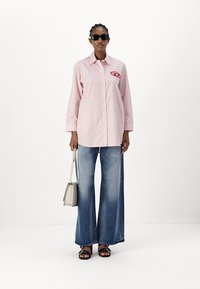 Red and white striped button-up shirt with long sleeves, paired with wide-leg blue denim jeans and black sandals. Holding a small beige bag.