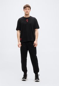 Μαύρο βαμβακερό T-shirt με κόκκινη γραφική λεπτομέρεια, συνδυασμένο με μαύρη φόρμα με χρυσά γράμματα· και τα δύο με άνετη εφαρμογή.