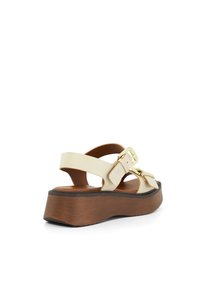 Beige platform sandalen met verstelbare banden, voorzien van een gouden gespaccent en een houten structuur in de zool voor extra stabiliteit.