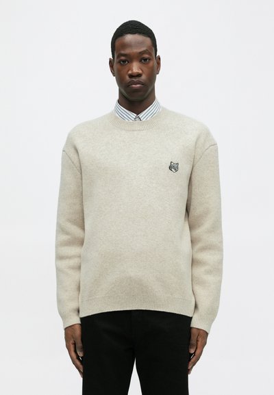 Gai brūns vilnas džemperis ar apaļu kakla izgriezumu, ribotām piedurknēm un apakšmalu. Priekšpusē ir izšūts pelēks lāča nospiedums.