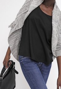 Grå stickad sjal med fransar, lager på ett enkelt svart linne. Blå jeans och en svart handväska syns också i bilden.