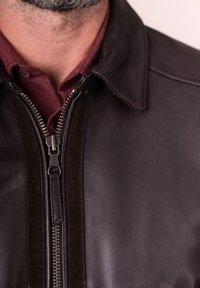 Close-up of a man’s neck and chest wearing a dark brown leather jacket zipped over a maroon collared shirt.