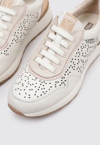 Zapatillas de piel blanca perforada con acentos en tono marrón, que presentan cordones planos y una etiqueta de marca en la lengüeta. Superficies texturizadas y suela de goma.