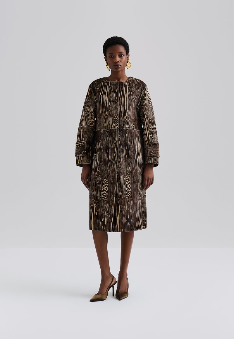 Vestido listrado em castanho e dourado com mangas longas, decote redondo e detalhes de botões. Textura suave, design até o joelho, combinado com sapatos de salto agudo.