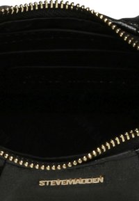 Indvendig i en sort læderhandtaske med flere rum, guld lynlåsdetailler og et sølv logo. Tekstureret stofforing.