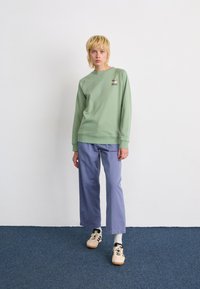 Sweatshirt vert clair avec des poignets côtelés et un petit motif floral sur la poitrine, associé à un pantalon lavender ample et des baskets de couleur claire.