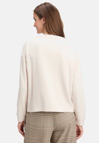 Jasny beżowy sweter z luźnym krojem, ściągaczami na rękawach i okrągłym dekoltem, zestawiony z kraciastymi spodniami w odcieniach brązu i beżu.