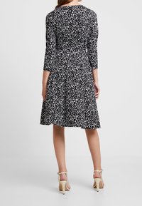 Mekko, jossa on musta-valkoinen kuviot, kolmivartiset hihat, tiukka yläosa, liisi hame ja pehmeä kangas. Korostettu korkeilla sandaaleilla.