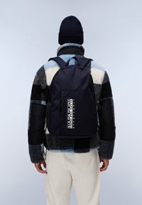 Zaino blu navy con un unico scomparto, caratterizzato da un grande logo e una tasca laterale in rete, abbinato a una giacca in pile multicolore e testurizzata.