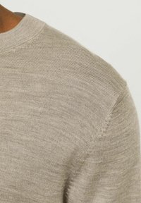 Maglione beige lavorato a maglia con scollatura rotonda, caratterizzato da una texture liscia e leggere costine lungo il colletto, che mette in mostra un design pulito.