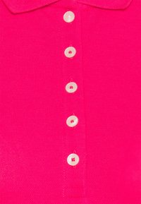 Fuchsiová polo košile s klasickým límcem a šesti kulatými bílými knoflíky po celé délce pro zapínání. Texturovaná pletenina.