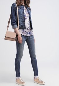 Jeansjacka, blommig blus, blå skinny jeans och sneakers i roséguld. Outfiten har lite slitningar och en ljusrosa axelväska.