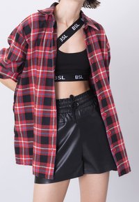 Rød og sort ternet oversized skjorte med korte ærmer, båret åben over en sort crop top og sorte shorts i kunstlæder med elastisk talje.