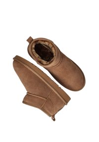 Bruine suède enkelboots met een zachte, met bont gevoerde binnenkant, ronde neus en een platte rubberen zool. Heeft een achterste lus voor gemakkelijk aan- en uittrekken.