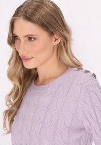 Maglione a coste di colore lilla con collo rotondo e bottoni metallici decorativi sulla spalla. Texture morbida e motivo dettagliato.