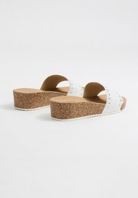 Sandalias de plataforma blancas con suela de corcho, diseño redondeado y dos correas diagonales con cortes redondos y detalles de textura sutiles.