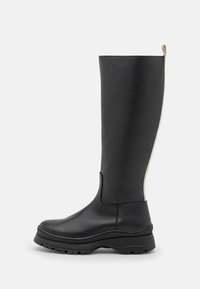 Bottes noires en cuir, montantes jusqu'au genou, avec une fermeture éclair contrastante crème, un bout arrondi et une semelle en caoutchouc texturé pour une meilleure adhérence et stabilité.