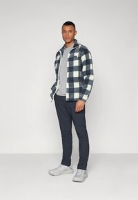 Herrejakke i marineblått og hvitt rutete flanell med hel glidelås, kombinert med en grå t-skjorte, mørkeblå bukser og hvite joggesko.