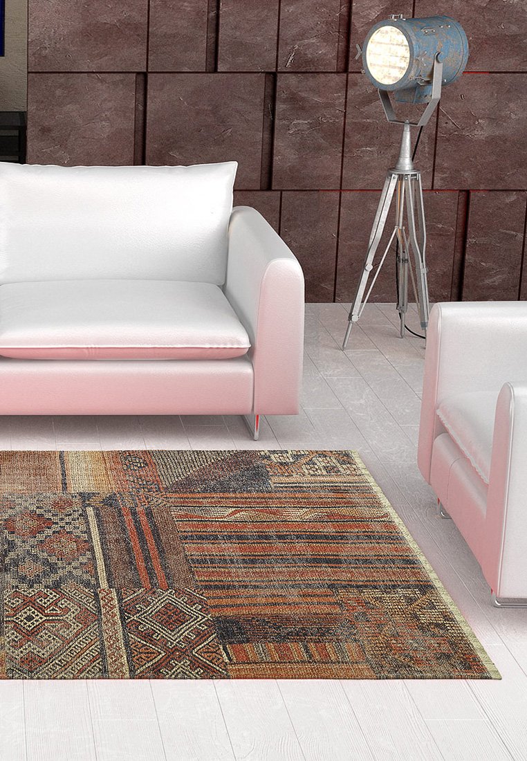 Wielokolorowy dywan z geometrycznymi wzorami w ziemistych odcieniach, o fakturze tkanej tkaniny, umieszczony na jasnej podłodze pod nowoczesnymi meblami.