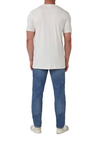 Witte kortemouwen T-shirt gemaakt van katoen, gedragen met lichtblauwe spijkerbroek en witte sneakers, gezien vanaf de achterkant.