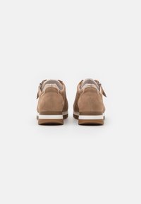 Brown suede sneakers with a rounded shape, white-striped sole, and zip closure detail. Smooth inner lining and cushioned heel.