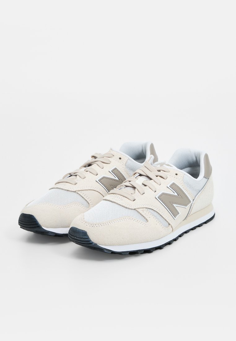Baskets de sport beiges en matériaux mesh et suède, avec un logo "N" gris, un design léger et une semelle extérieure noire texturée.