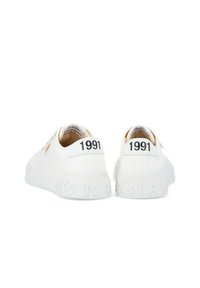 Sneakers bianchi con suola testurizzata, caratterizzati dalla scritta nera "1991" sul tallone e design minimalista. Materiale in tela, lacci piatti.