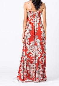 Dlouhé červené květinové šaty s bílými vzory, nastavitelné tenké ramínka, řasený korzet a volánková sukně, vyrobené z lehkého materiálu.