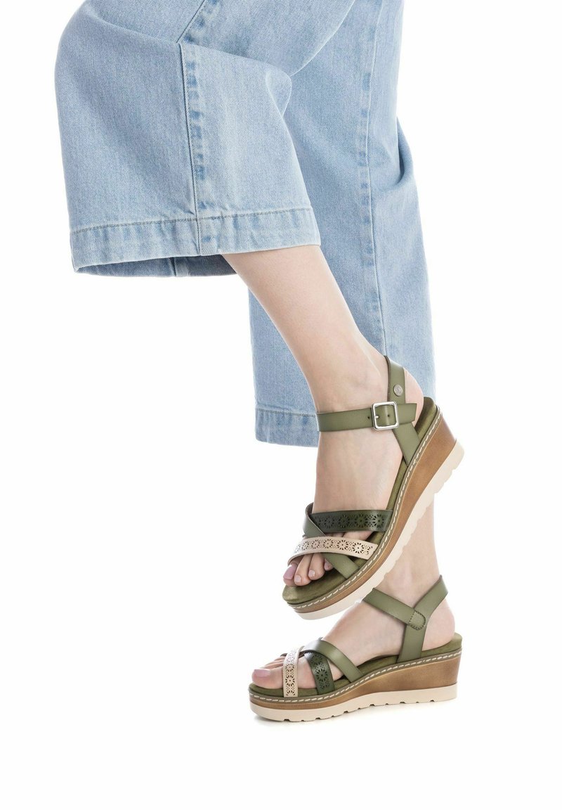 Sandalias verdes de cuña con diseño de correas cruzadas, acentos decorativos perforados y una suela de plataforma en color tostado, vistas de lado.