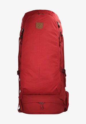 Mochila vermelha em nylon com formato retangular, alças laterais ajustáveis e fecho de zíper no topo. Apresenta um emblema de couro castanho.