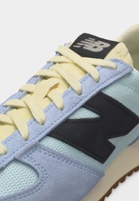 Gros plan d'une basket bleu clair et jaune avec des lacets jaunes et un logo New Balance noir sur le côté.