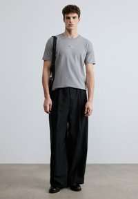 Γκρίζο βαμβακερό T-shirt με στρογγυλή λαιμόκοψη και λογότυπο, συνδυασμένο με μαύρο, φαρδύ παντελόνι και μαύρα παπούτσια. Απλή, καθημερινή εμφάνιση.