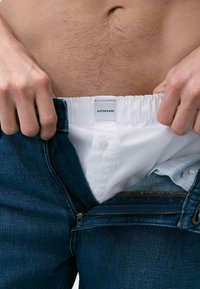 Dżinsy z zamkiem błyskawicznym i guzikami, z białym, elastycznym paskiem w talii z metką "AUTOGRAPH" oraz jasnym koszulą pod spód.