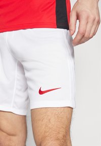 Weiße sportliche Shorts mit rotem Nike-Swoosh-Logo, aus leichtem Material gefertigt, mit texturiertem Finish und Seitenschlitz für Bewegungsfreiheit.