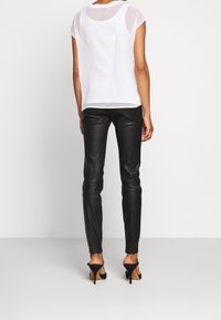 Bílý průsvitný top s krátkými rukávy v kombinaci s černými přiléhavými koženými kalhotami a černými lodičkami na podpatku. Hladké textury s minimalistickým designem.