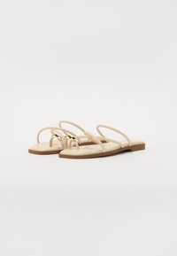 Beige flade sandaler med fine stropper og en guldfarvet detalje på den centrale strop. Blød tekstur med et minimalistisk design. Flad sål.