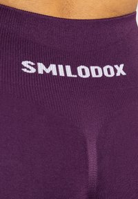Leggings viola senza cuciture caratterizzati da una texture a maglia stretta e un logo bianco "SMILODOX" sulla cintura. Vista ravvicinata dei dettagli del tessuto.