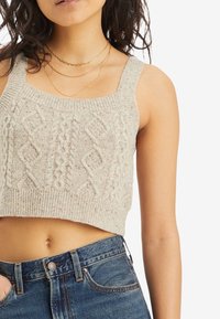 Light grey knitted crop top with a textured cable pattern and wide straps, paired with high-waisted blue denim jeans.