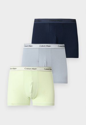 Tre Calvin Klein herre-bokserbriefs i navy, lys grå og bleg gul med mærkede taljebånd på ensfarvet baggrund.