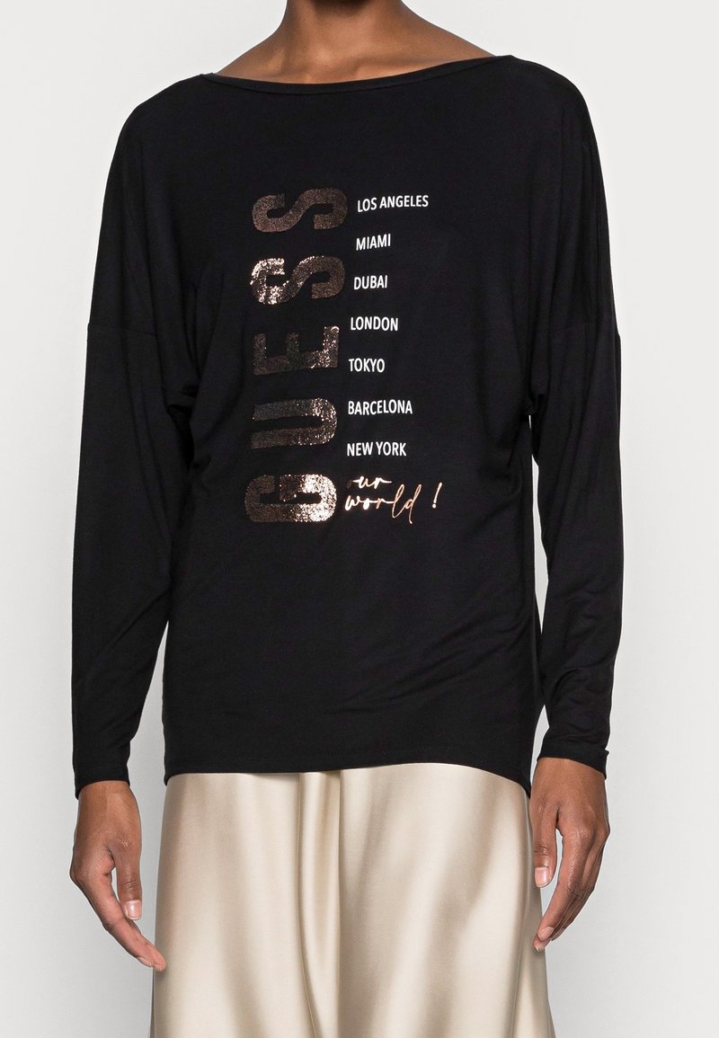 Schwarzes Langarm-T-Shirt mit metallischen Buchstaben, die "GUESS" und Städtenamen buchstabieren. Weicher Stoff mit lockerer Passform und Bootsausschnitt.