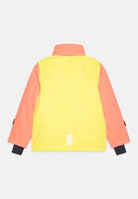 Gul och korallfärgad långärmad jacka med hög krage, svarta innerärmar och en liten reflexdetalj nära nedre ryggen.