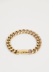 Pulsera de cadena de oro con grandes eslabones entrelazados. El cierre incluye un logotipo con acentos de rayas en rojo, blanco y azul. Textura suave.