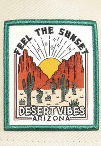 Gesticktes Patch mit roten Felsformationen, einer gelben Sonne, Kakteen und dem Text "FÜHL DIE SONNENUNTERGANG-WÜSTENVIBES ARIZONA" auf einem weißen Hintergrund.