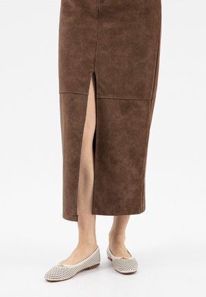 Bruine midi-rok met voorsplit die blote benen laat zien, gecombineerd met witte geperforeerde ballerina's met een klein strikdetail.