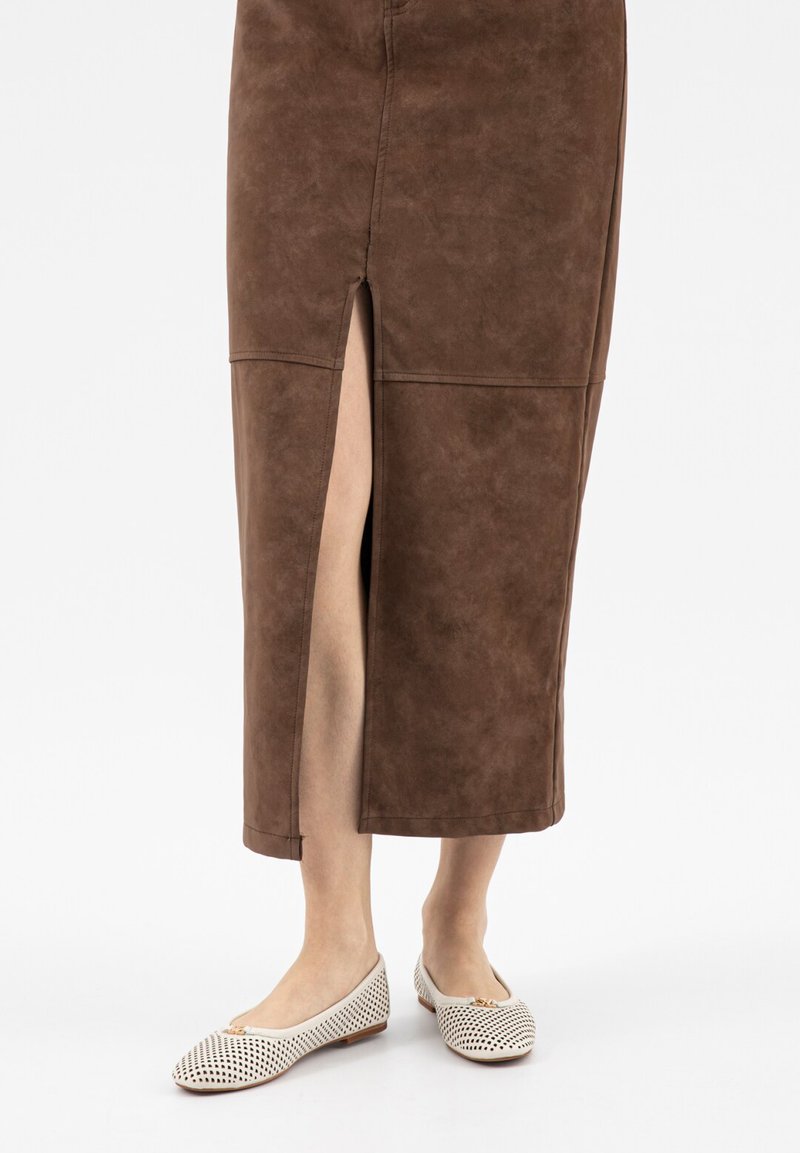 Gonna midi marrone con spacco frontale che mostra le gambe nude, abbinata a ballerine bianche traforate con piccolo dettaglio a fiocco.