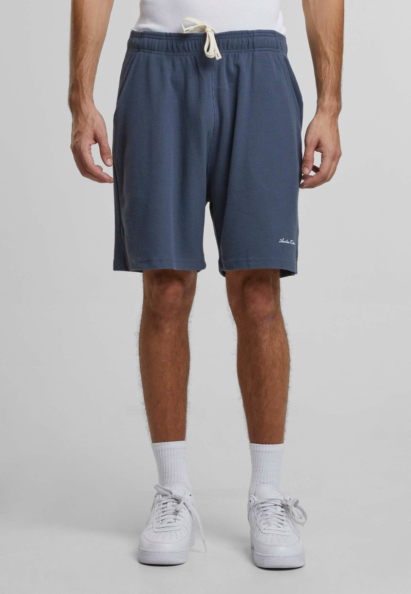 Shorts texturate de culoare albastru închis cu un elastic la talie și șnur. Prezintă buzunare laterale și un accent cu logo aproape de tiv.