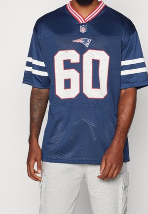 Man wearing a navy blue New England Patriots NFL jersey with number 60 and gray cargo pants, standing against a plain background.