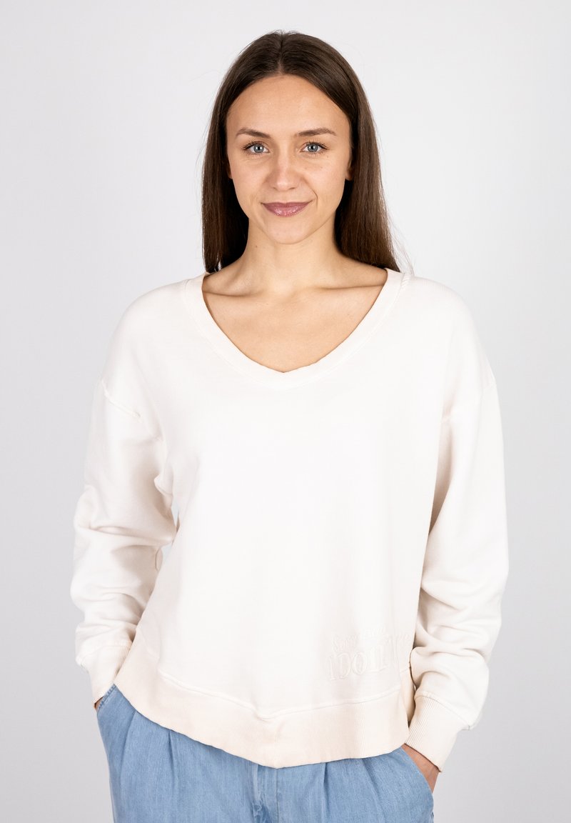 Cream v-neck sweatshirt in soft fabric with a relaxed fit. Features embroidered text at the hem and cuffed long sleeves.